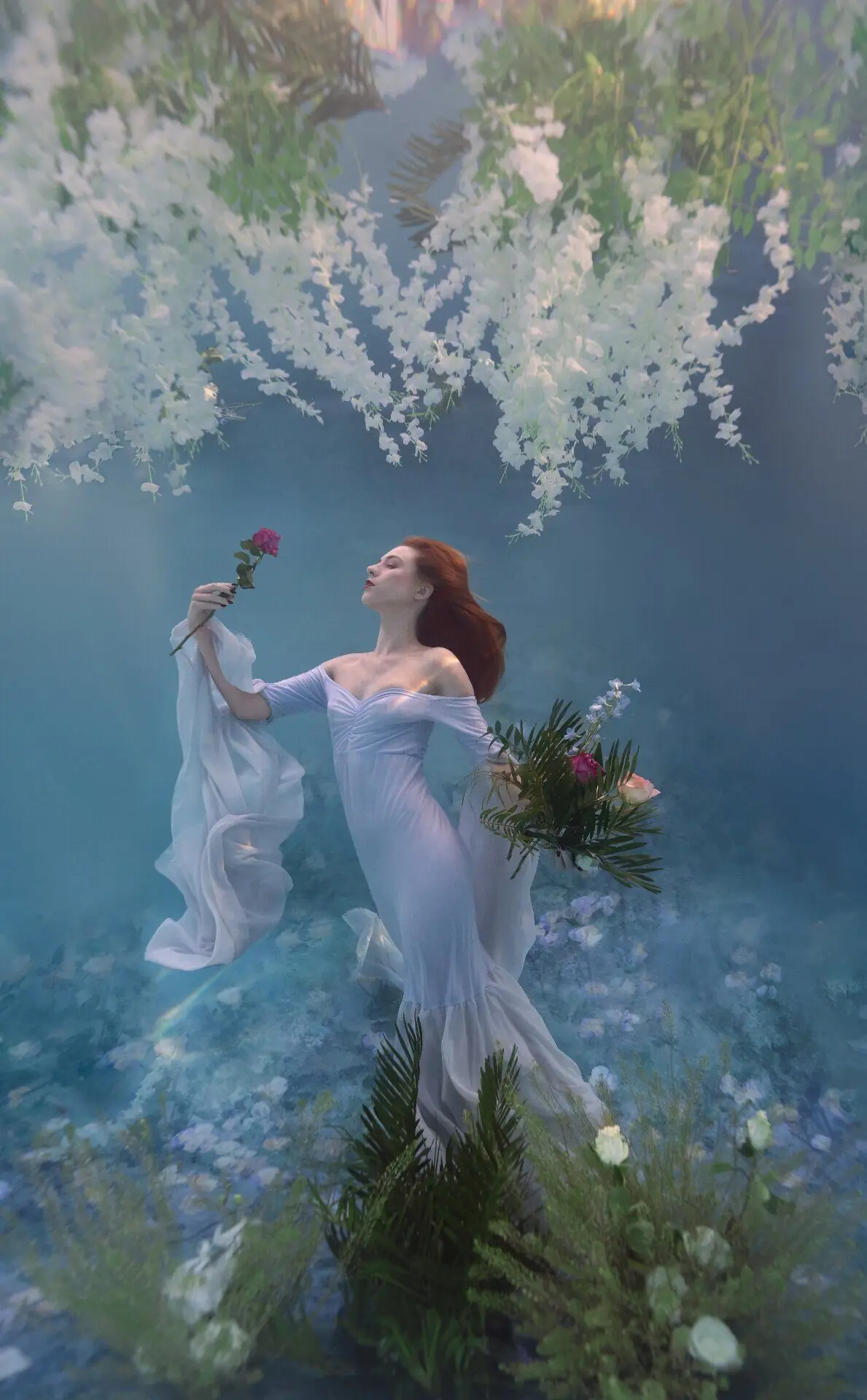 Woman floating in water surrounded by colorful flowers during an underwater portrait photography session with Water Bear Photography