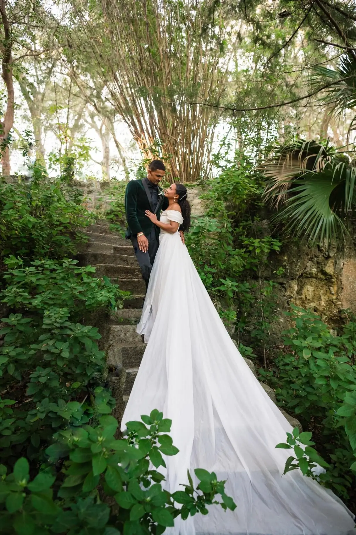 Wedding couple on stone steps surrounded by lush greenery